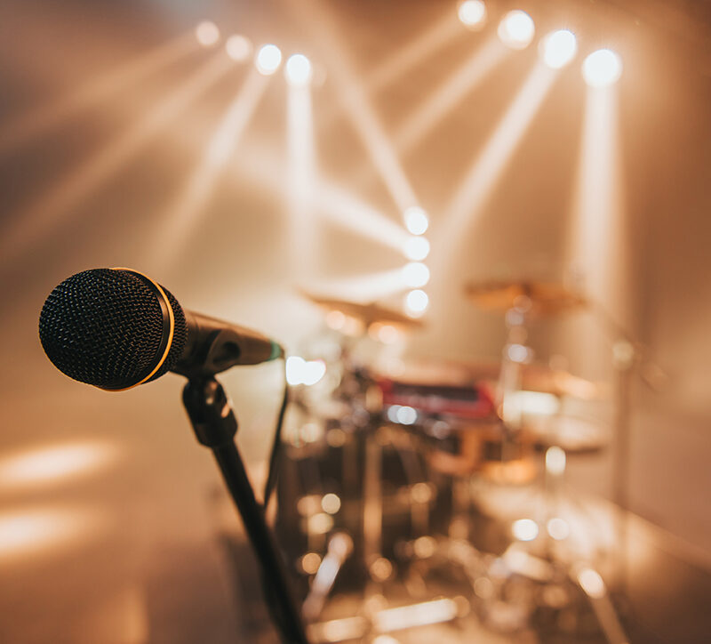 Microphone on a stage with a drum set and orange lights in the background on a concert